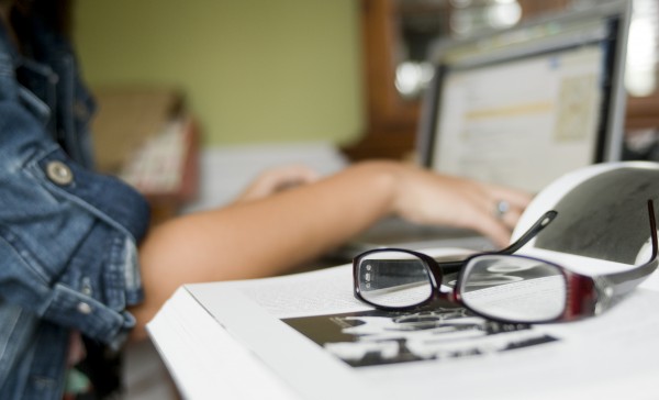 A student on a laptop with a pair of glasses in the forefront.