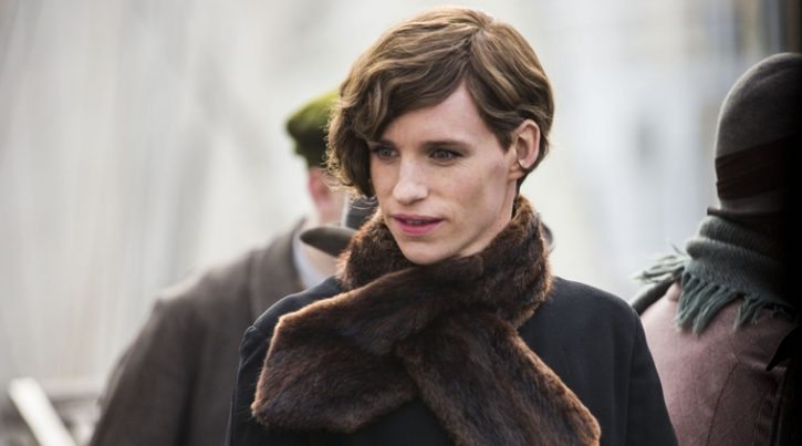 Eddie Redmayne is dressed in drag, with red lipstick on and his hair in a short, curled style. He wears a fur scarf around his neck.