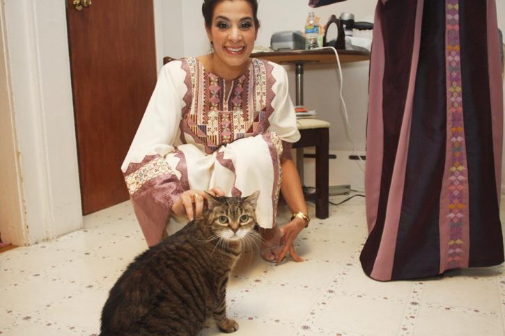 Maysoon is kneeling down, smiling at the camera, as she puts her hand on her cat Lucy.